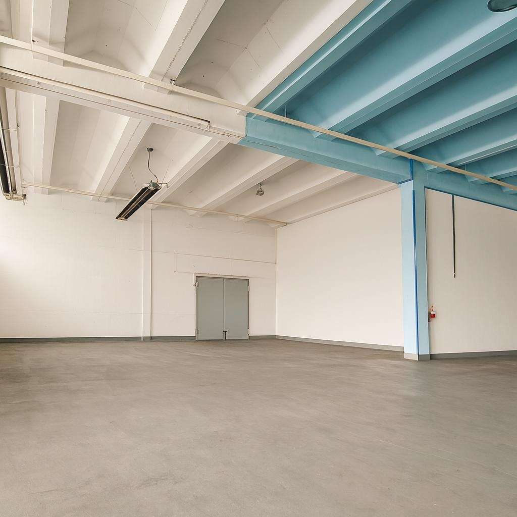 Empty industrial warehouse interior with white walls, gray double doors at the far wall, and blue steel beams supporting the ceiling.