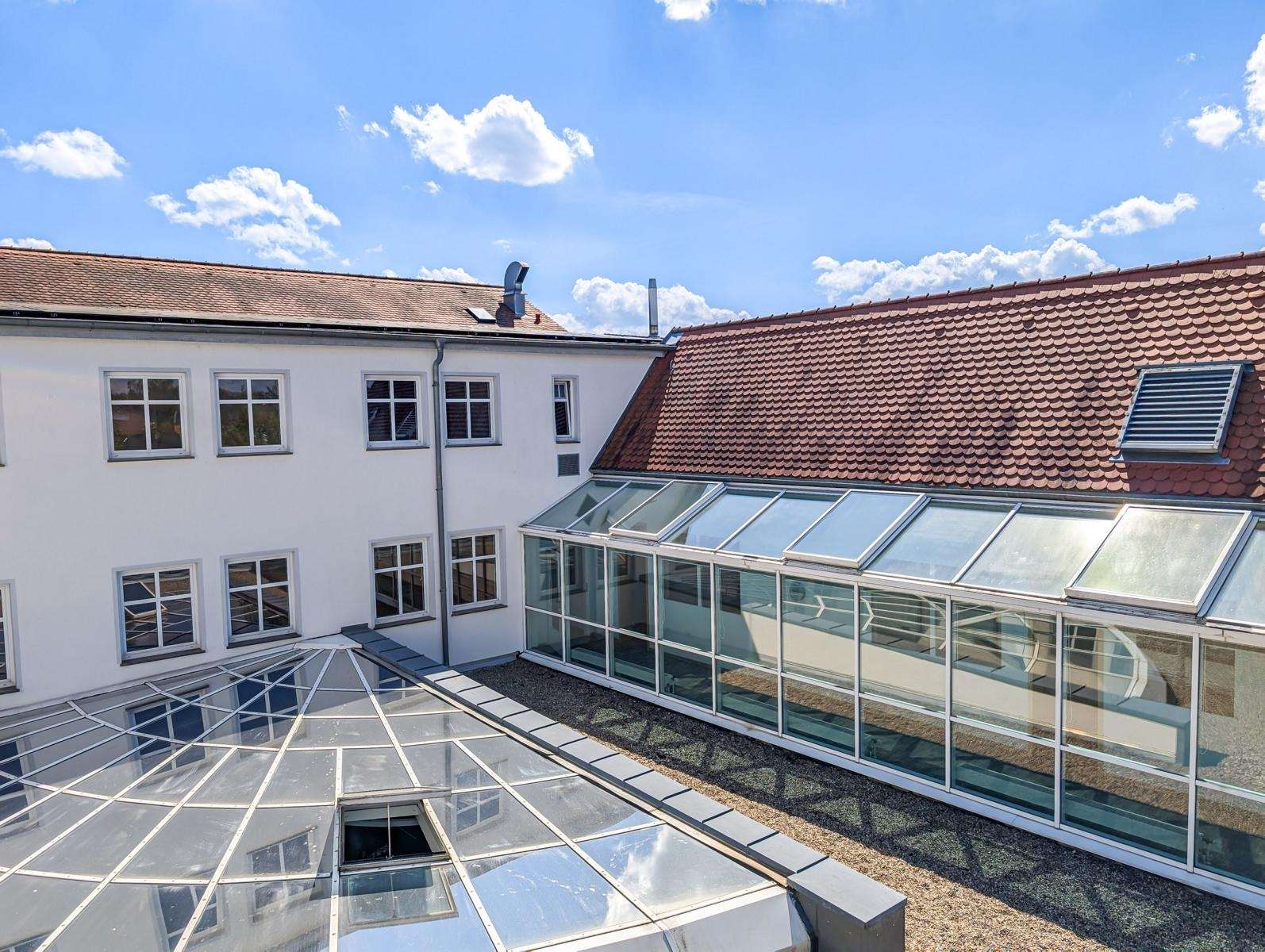 Courtyard of a white building with a glass-paned conservatory and red-tiled roof under a bright blue sky.