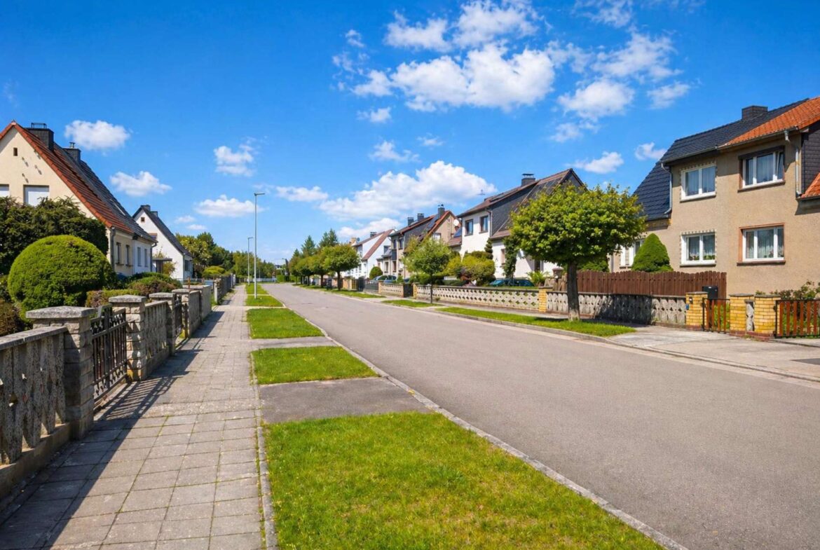 Residential street with row of neat houses, green lawns, and a clear blue sky above.
