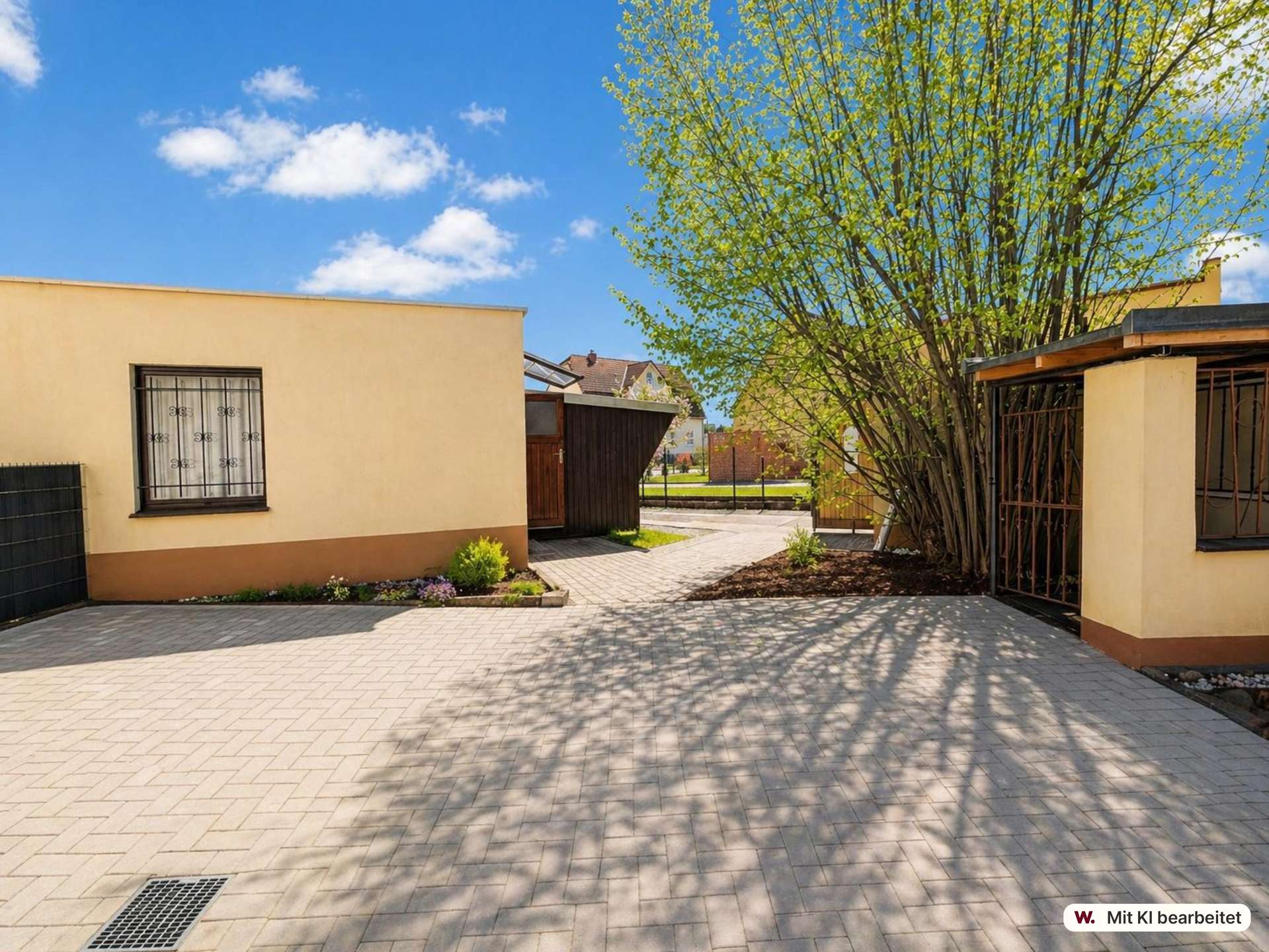 Courtyard scene with beige buildings, a large tree, and a paved brick walkway under a blue sky.
