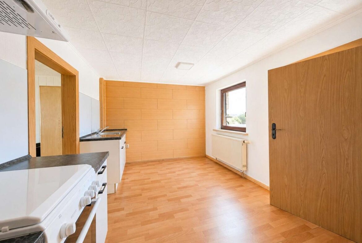 Bright kitchen with light wood cabinets, white appliances, and a large window bringing in natural light.