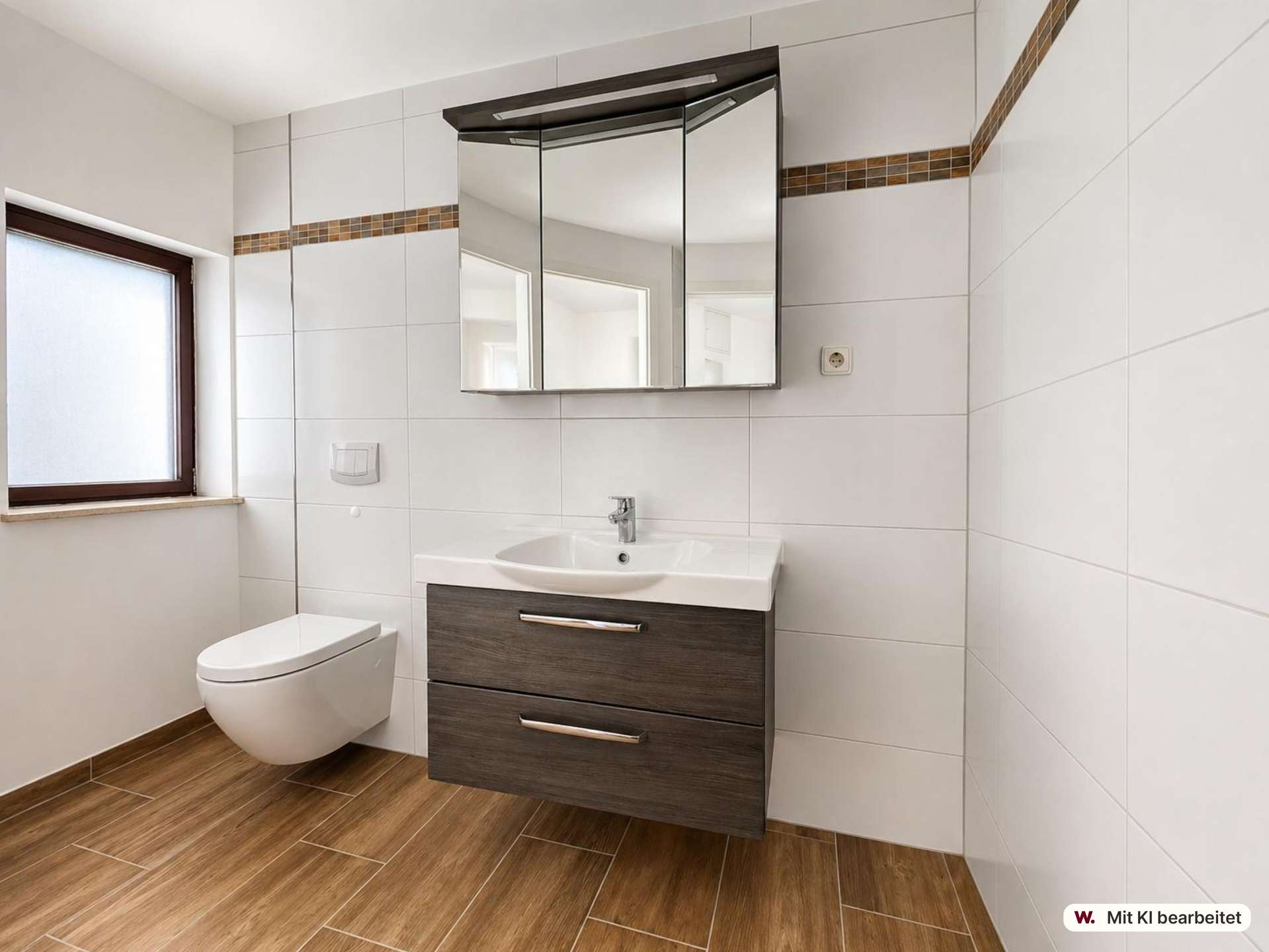 Modern bathroom with a wall-hung toilet, dark wood vanity, and a three-panel mirrored cabinet above a white sink. White tiled walls with brown mosaic trim, and a window to the left.