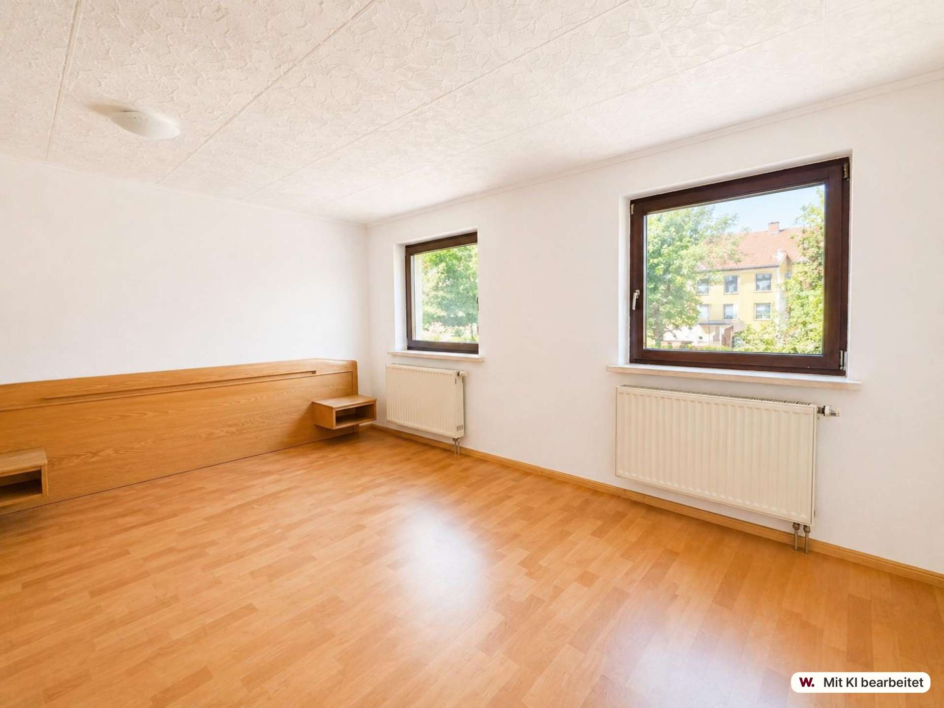 Bright empty bedroom with light wood floor, built-in wooden bed frame, and two large windows..Window view shows trees outside (radiators underneath).