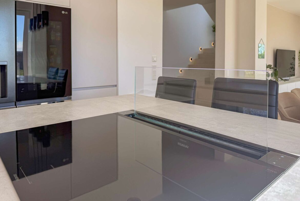 Contemporary kitchen with an island and a glass divider, stainless appliances, and light-colored surfaces.