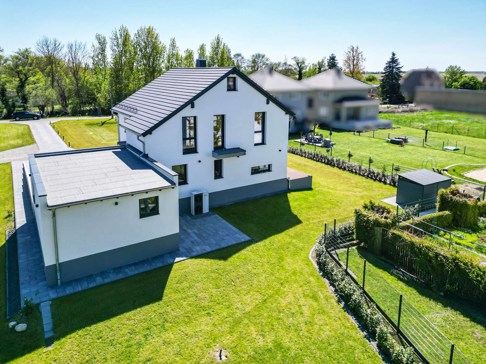 Aerial view of a modern white two‑story house with a dark roof, surrounded by a green lawn and a fenced yard.
