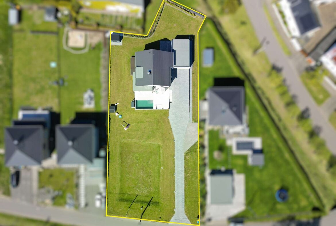 Aerial view of a residential property outlined in yellow, showing a large gray-roofed house and lawn.