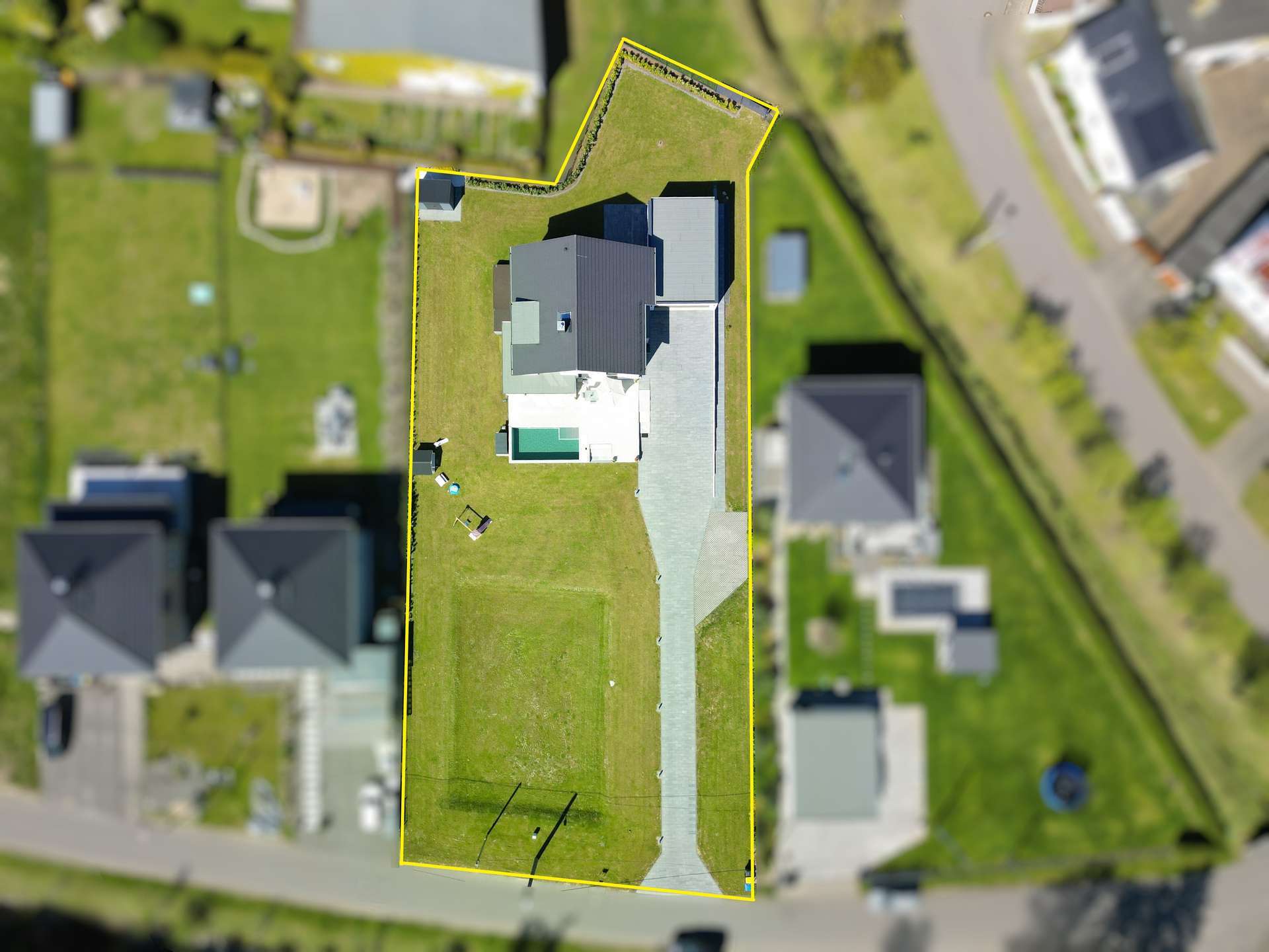 Aerial view of a residential property outlined in yellow, showing a large gray-roofed house and lawn.