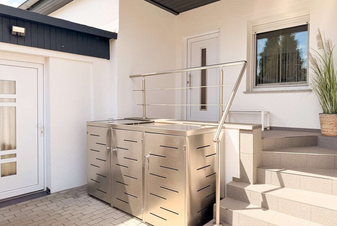 Outdoor stainless steel barbecue grill cabinet beside entry stairs on a modern white house porch.