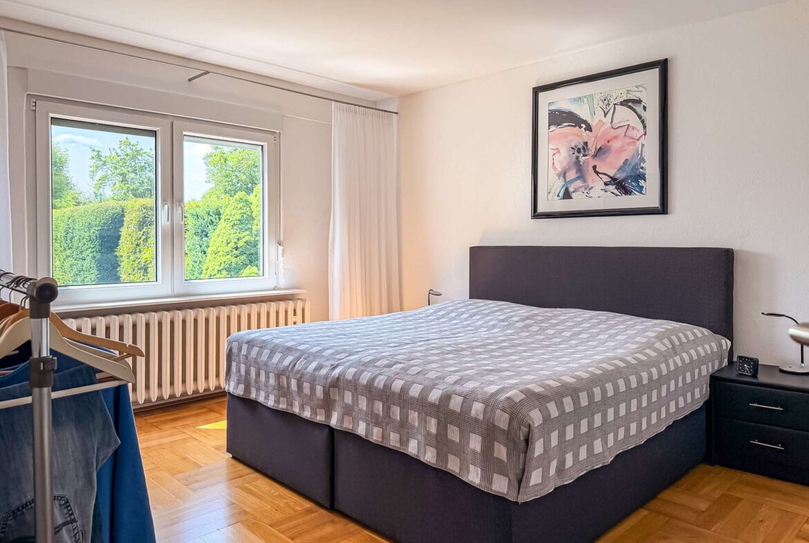 Bedroom with a double bed, gray checkered duvet, and a framed abstract painting above the headboard.