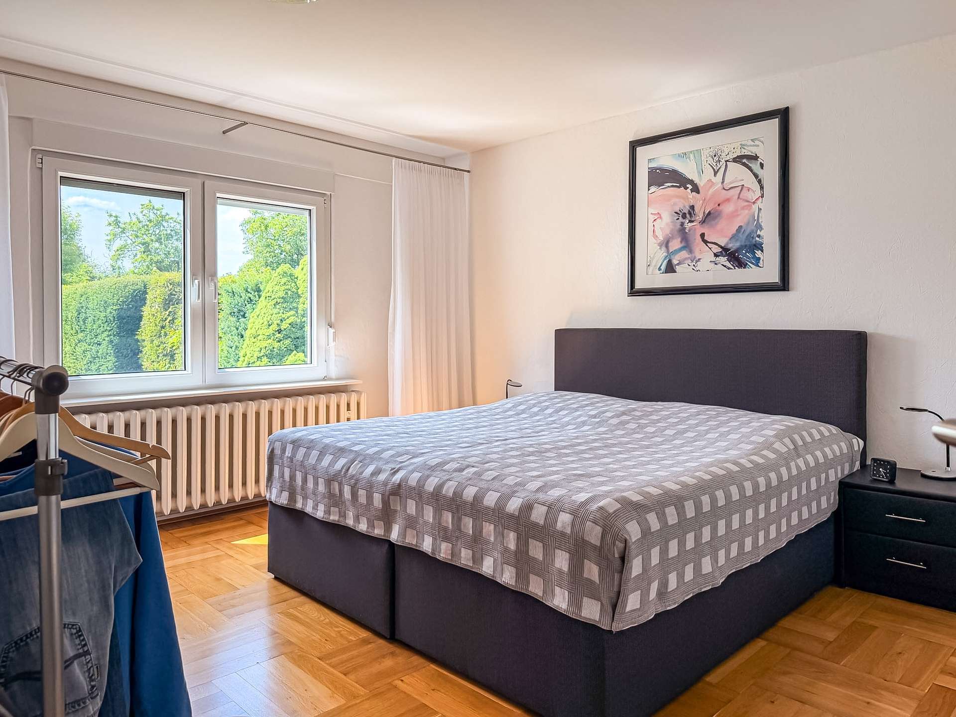 Bedroom with a double bed, gray checkered duvet, and a framed abstract painting above the headboard.