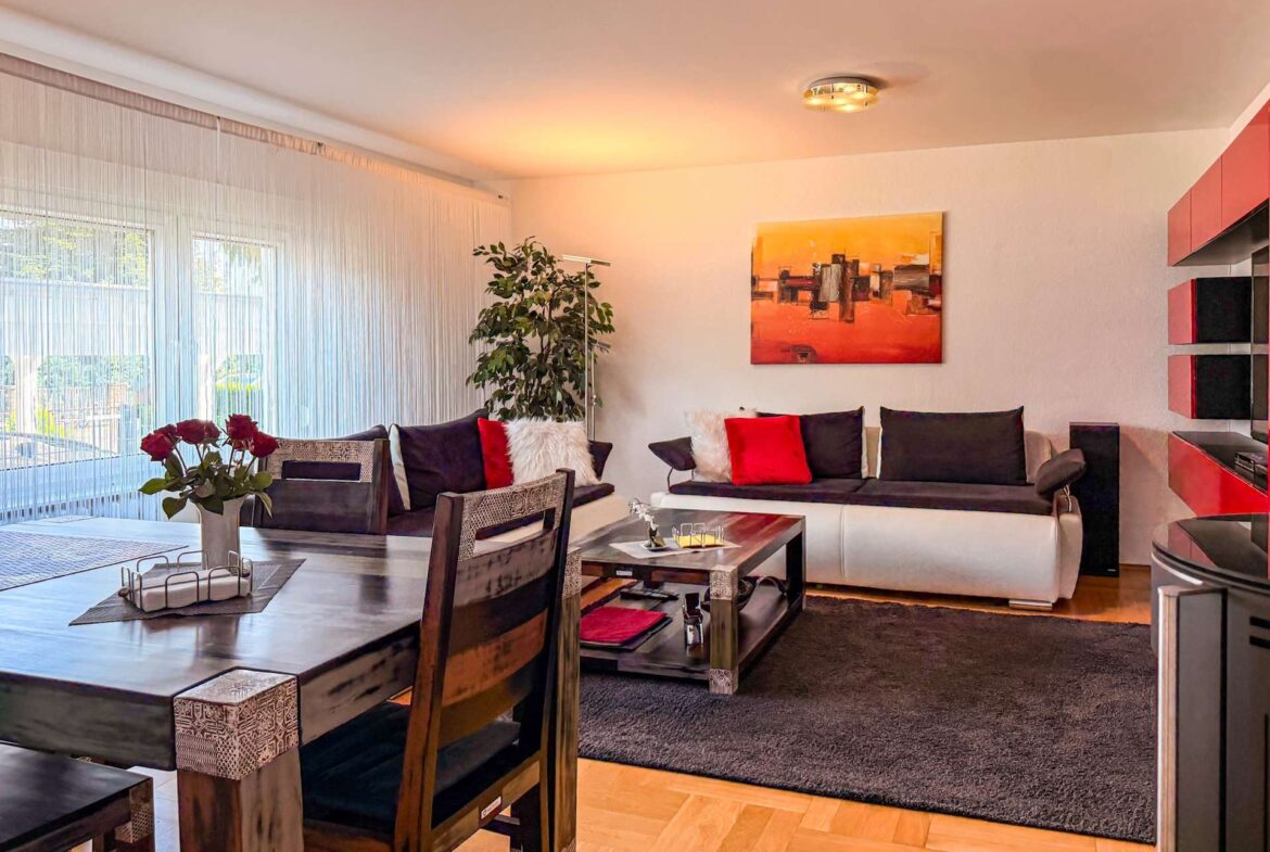 Bright living room with a dark wood dining set, red and black cushions, and an abstract orange painting on the wall.