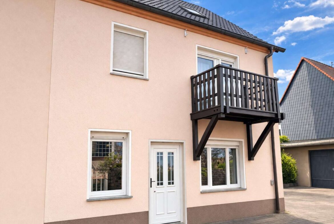 Two-story peach house with white-framed windows and a black wooden balcony on the second floor under a blue sky.