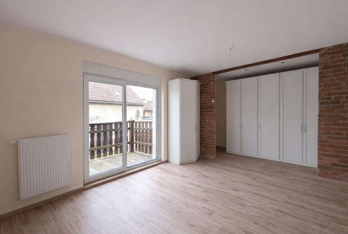 Bright living area with white built-in wardrobes along a brick wall and a sliding glass door to a balcony/yard beyond.