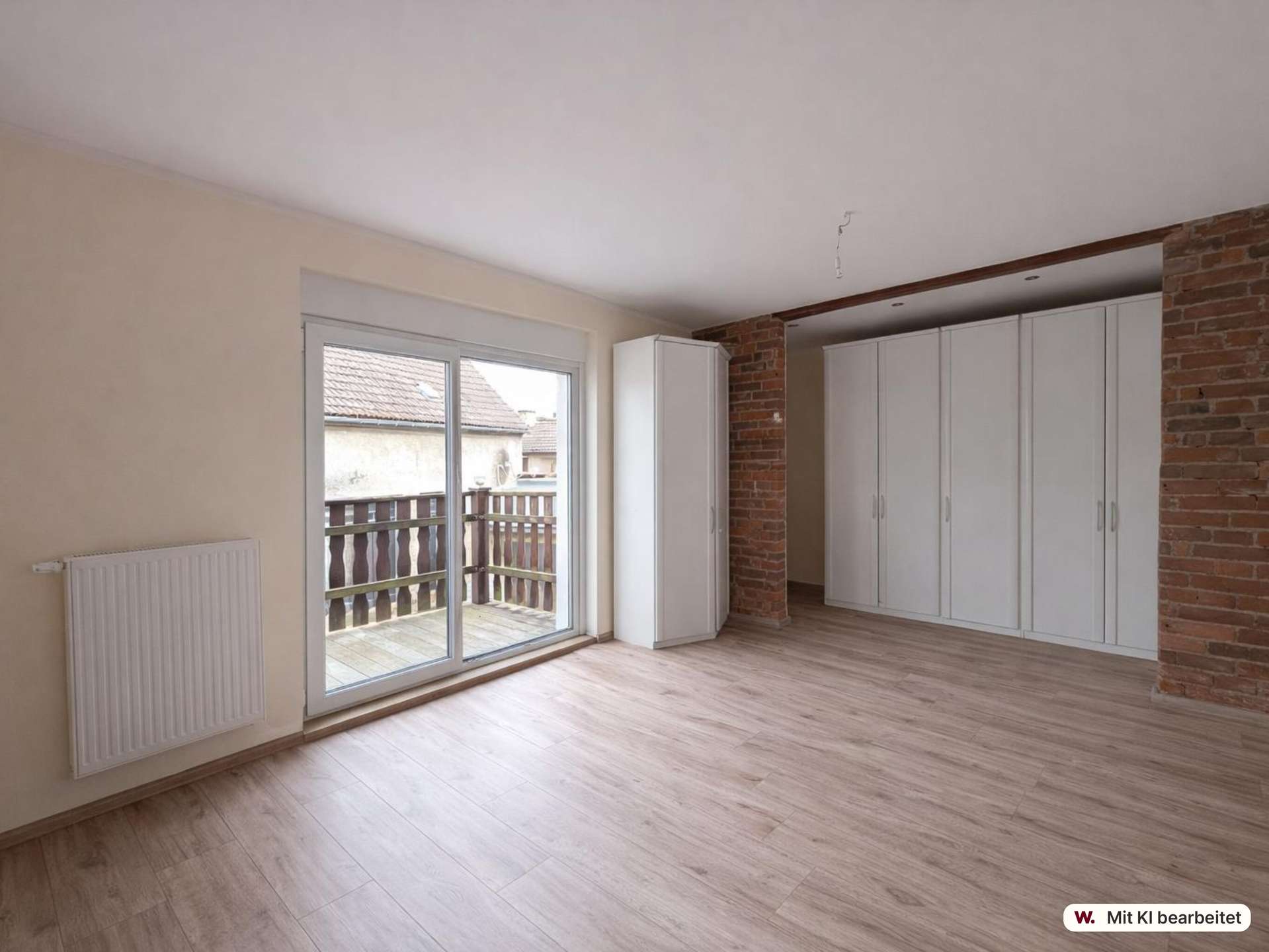 Bright living area with white built-in wardrobes along a brick wall and a sliding glass door to a balcony/yard beyond.