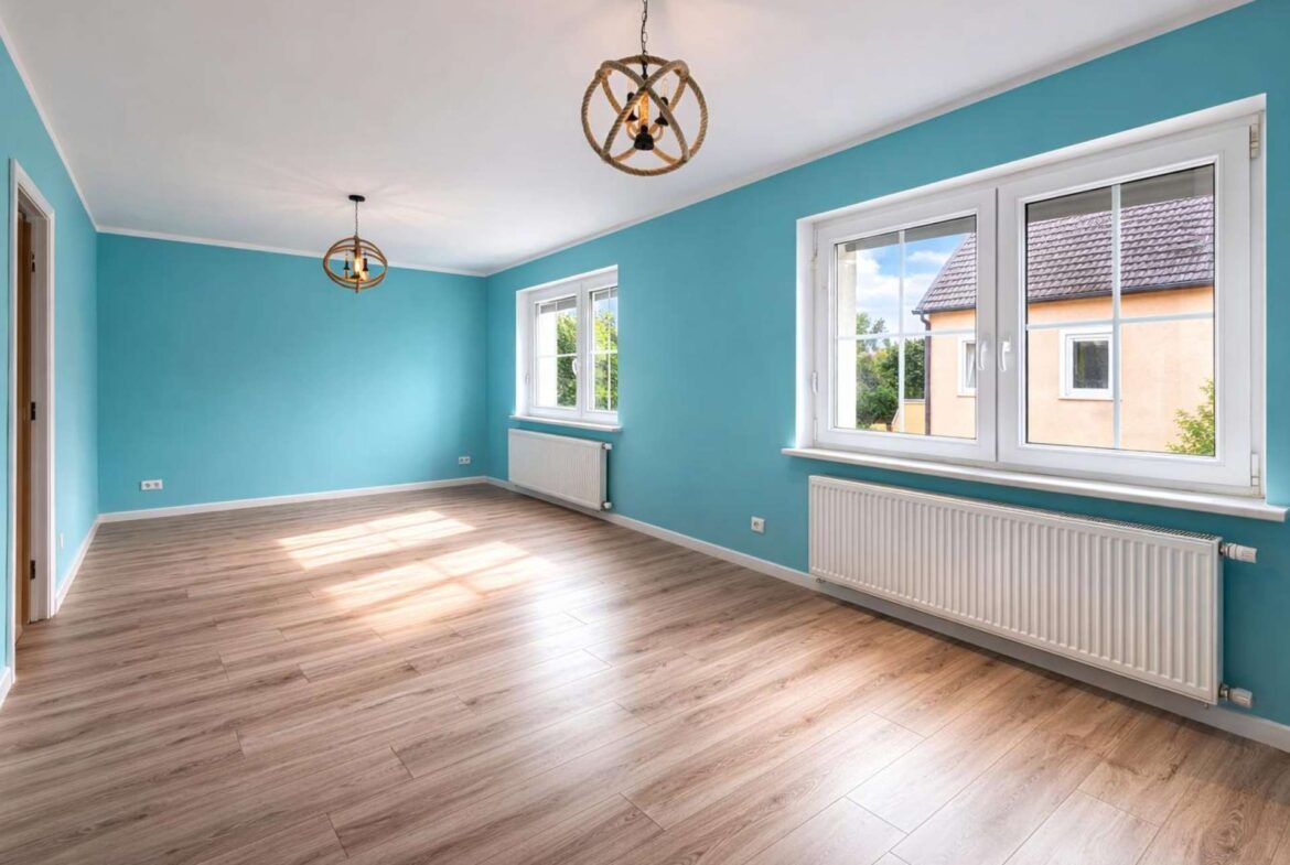 Bright, empty room with teal walls, light wood flooring, and two knot-rope pendant lights hanging from the ceiling.