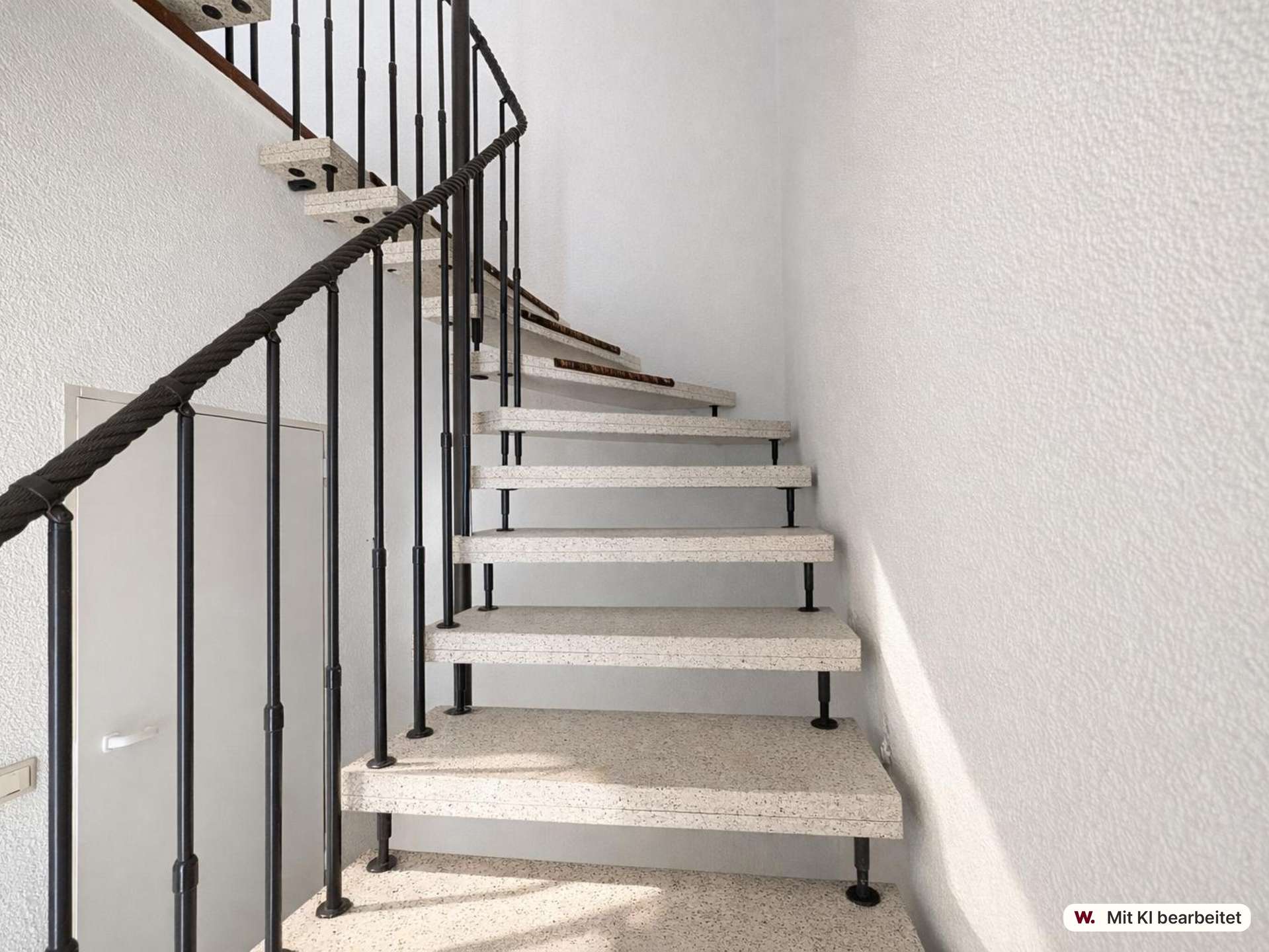 Interior spiral staircase with black metal railing and white speckled steps, ascending along white textured walls in a bright stairwell.