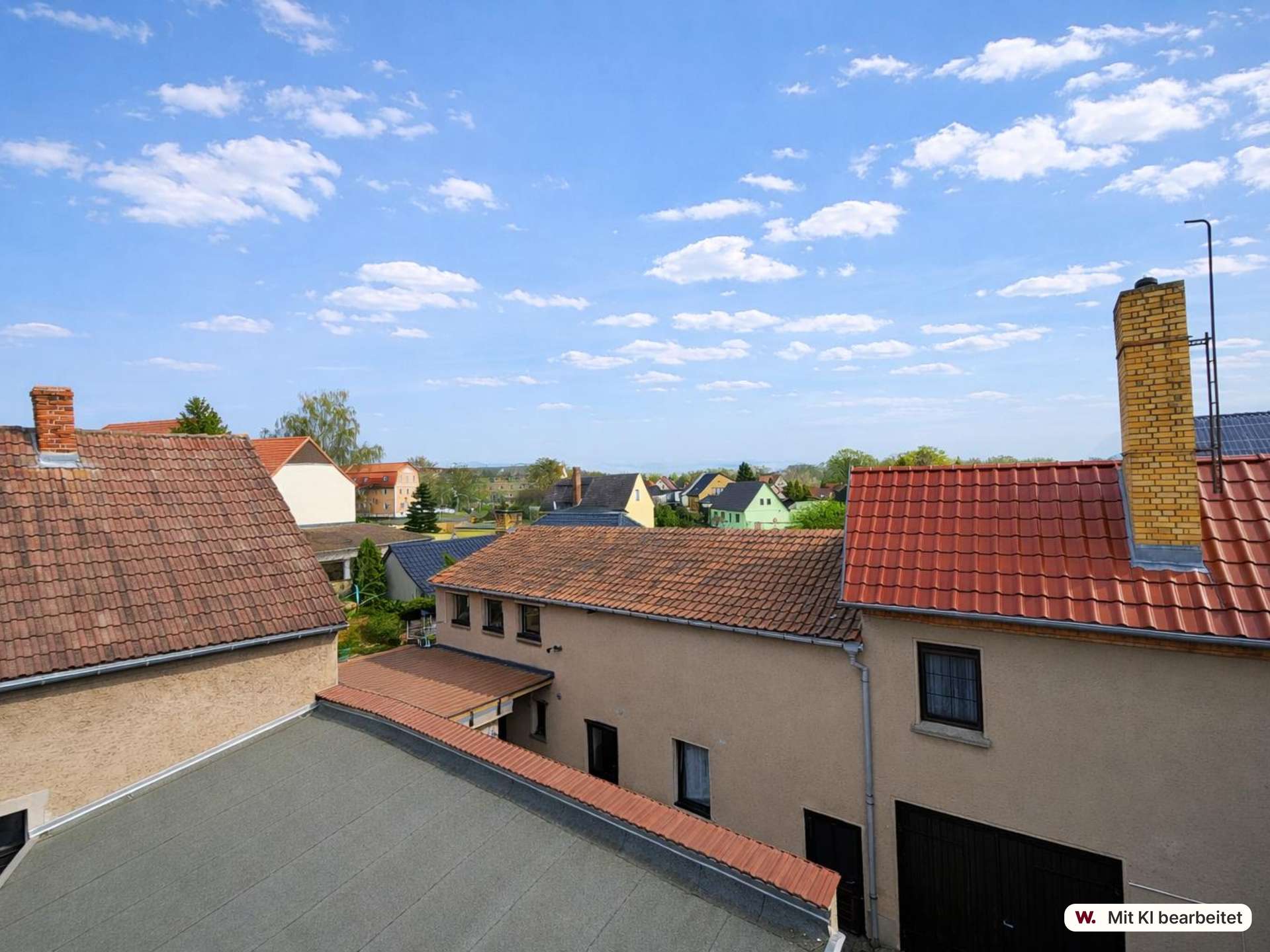 Aerial view of a suburban neighborhood with tiled roofs, brick chimneys, and a blue sky with scattered clouds.