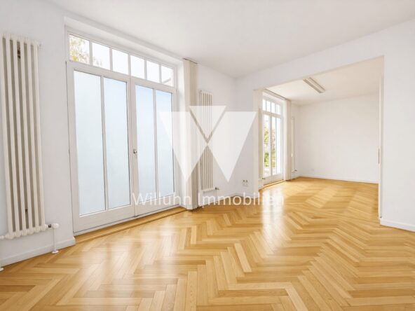 Bright, empty living room with white walls, herringbone parquet floors, tall radiators, and large glass doors to the outside patio/yard.
