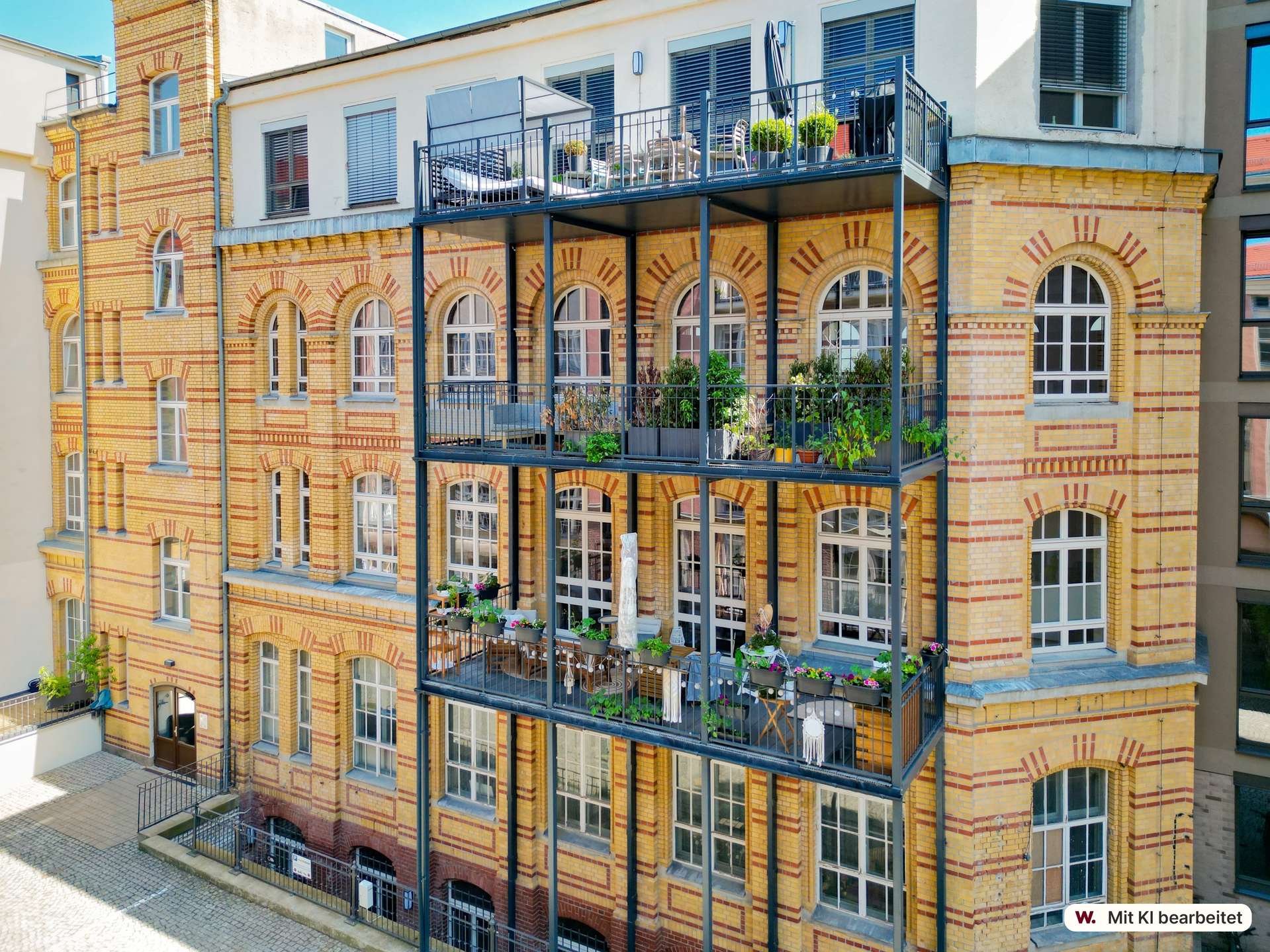 Historic yellow-brick apartment building with arched windows and black metal balconies adorned with plants and seating on each floor.