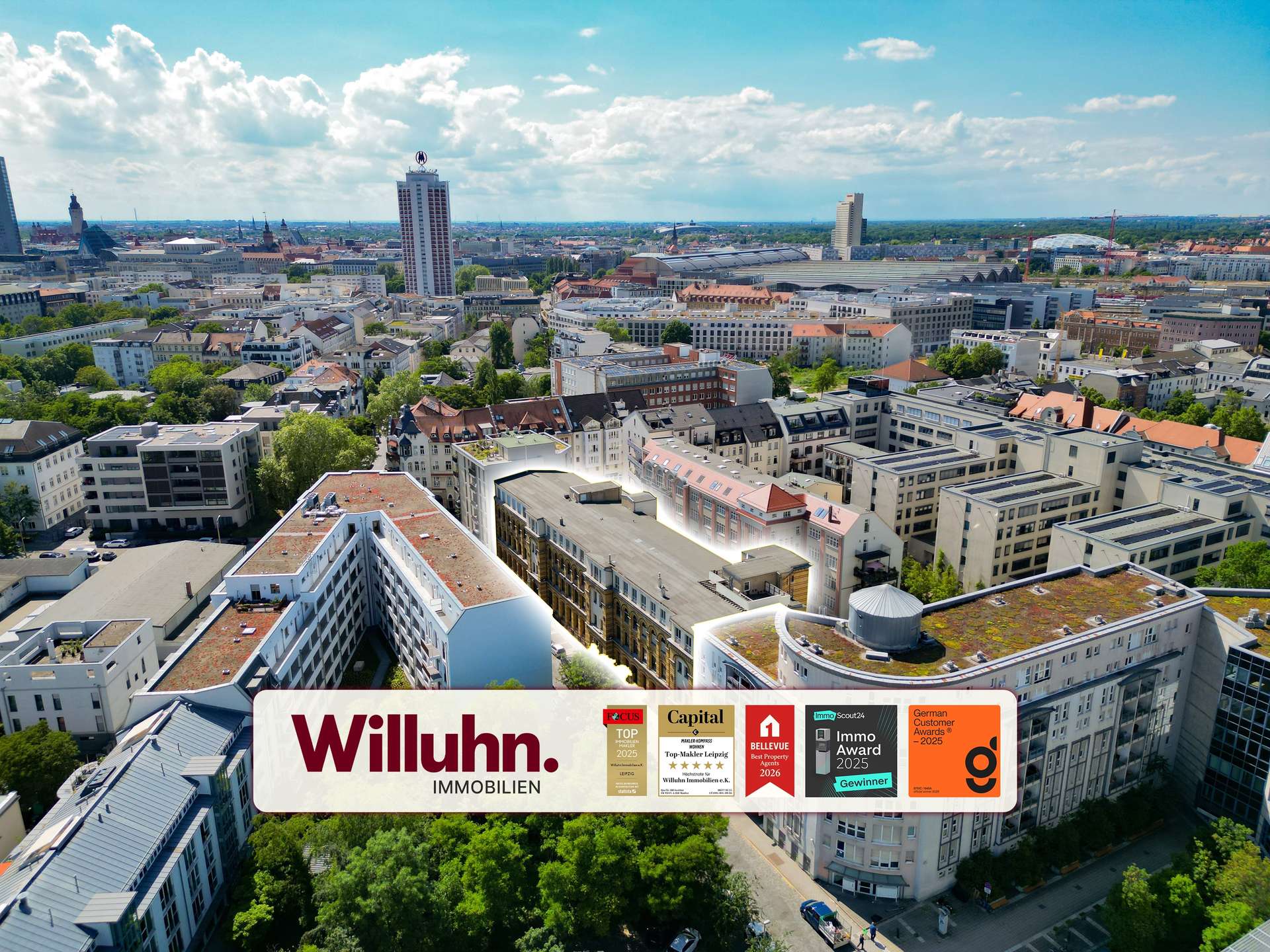 Aerial view of a European city with a large Willuhn Immobilien billboard across the bottom foreground, showing award logos.