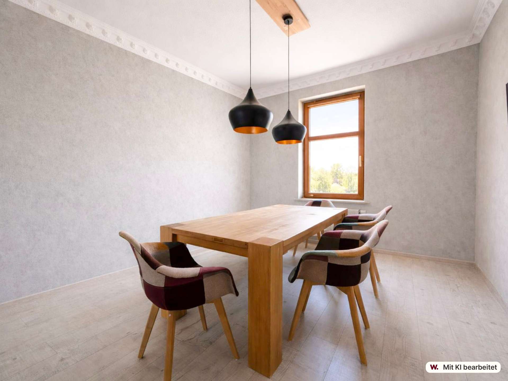 Wooden dining table surrounded by patchwork chairs in a bright room with gray walls and two black pendant lamps near a window.