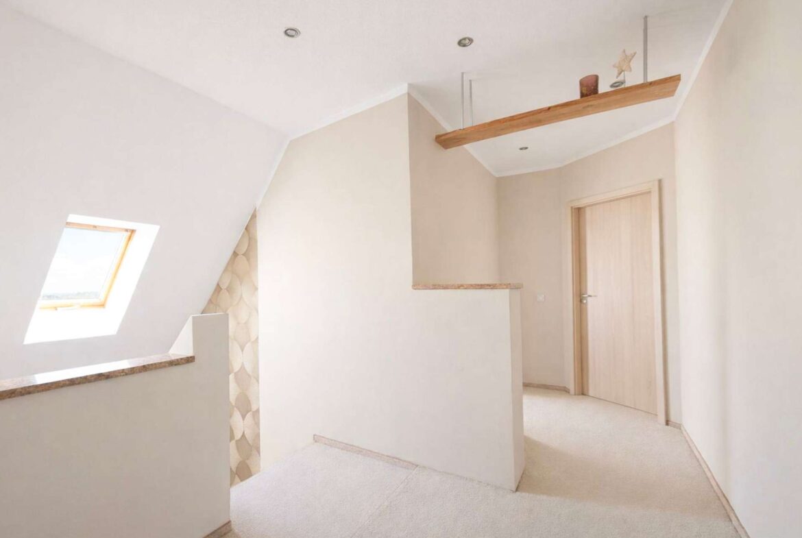 Bright beige hallway with a sloped ceiling, skylight window, and a floating wooden shelf near the ceiling.