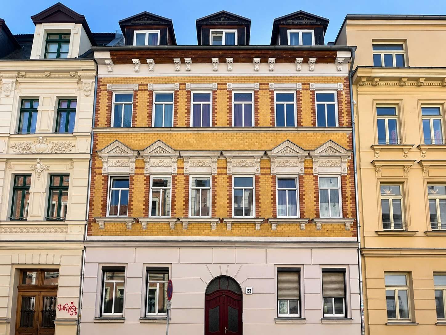Yellow brick townhouse with ornate white stone trim and tall windows on a city street, blue sky above.