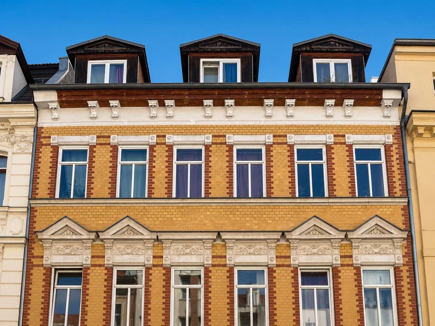 Brick building with decorative white stone trim and tall rectangular windows under a clear blue sky. They appear as an urban townhouse with ornate detailing at the lower facade and brick patterning.