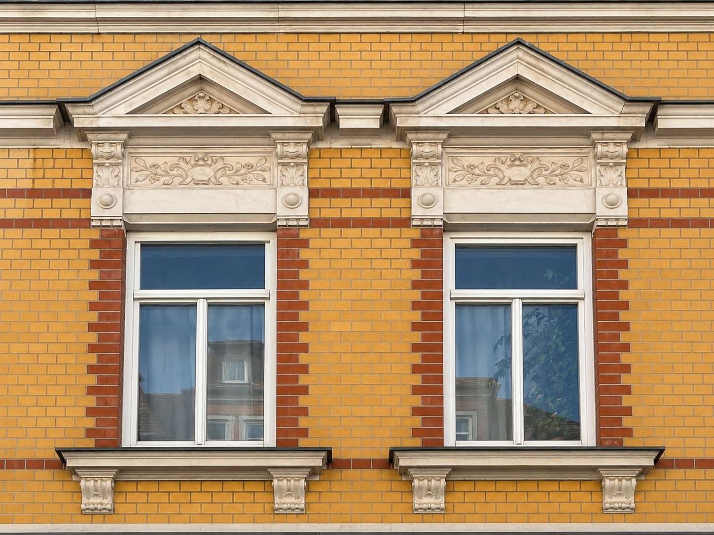 Two white-framed windows on a yellow brick facade with ornate white stone trim and triangular pediments above.