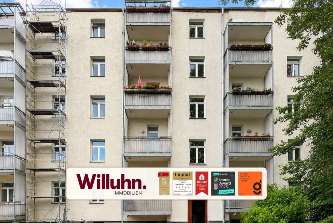 Facade of a beige apartment building with balconies and a large Willuhn Immobilien sign at ground level.