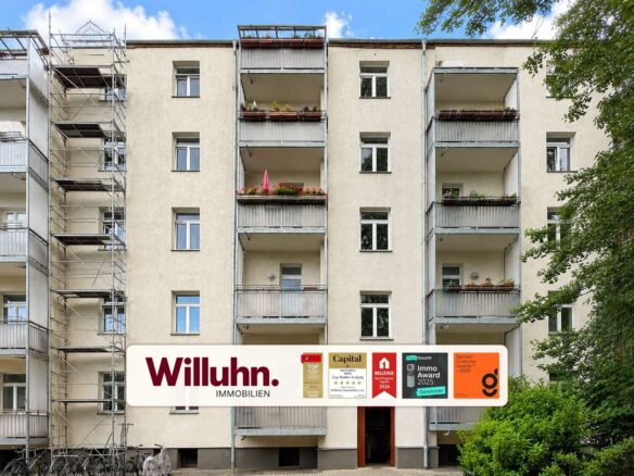 Facade of a beige apartment building with balconies and a large Willuhn Immobilien sign at ground level.