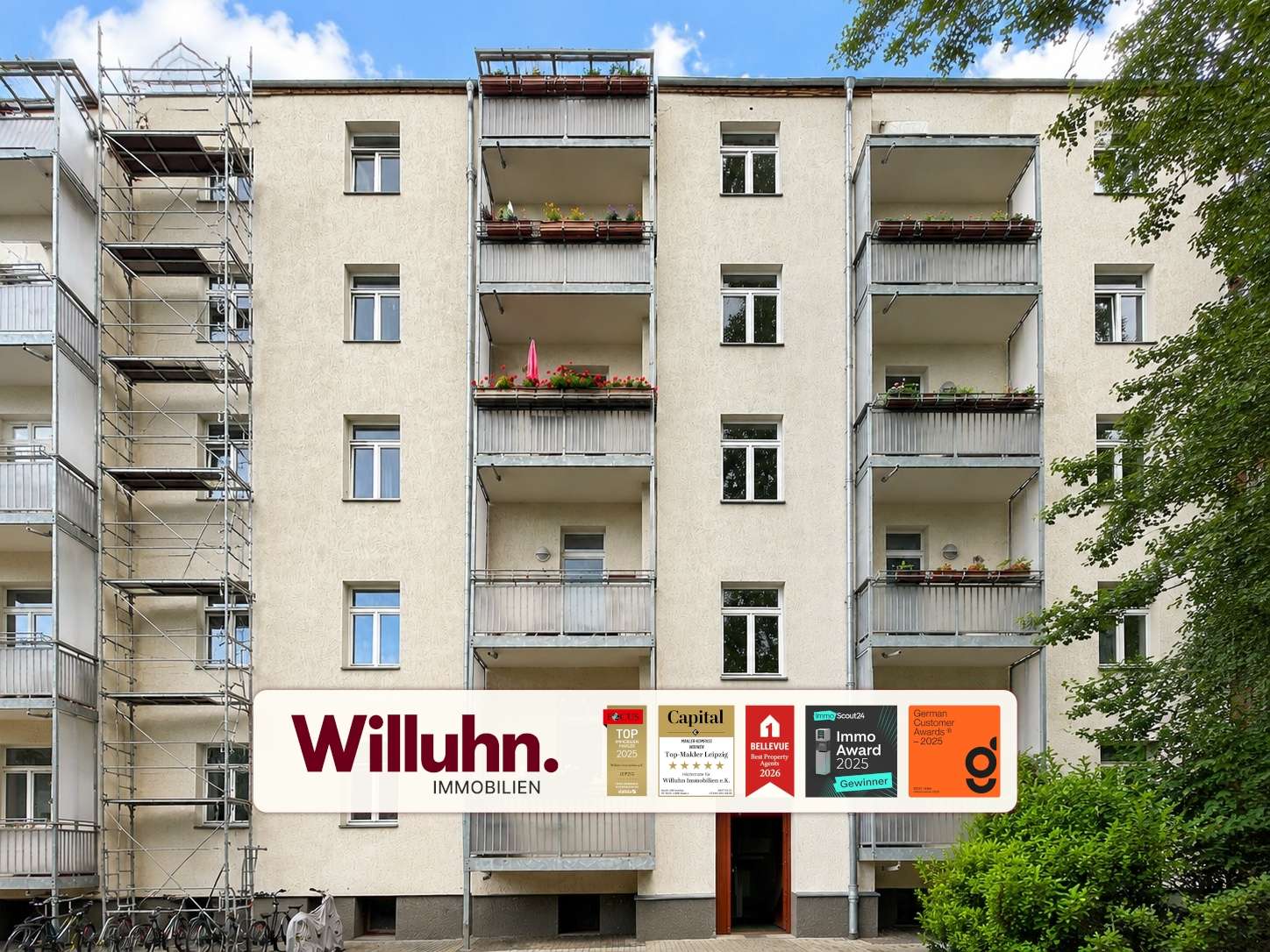 Facade of a beige apartment building with balconies and a large Willuhn Immobilien sign at ground level.