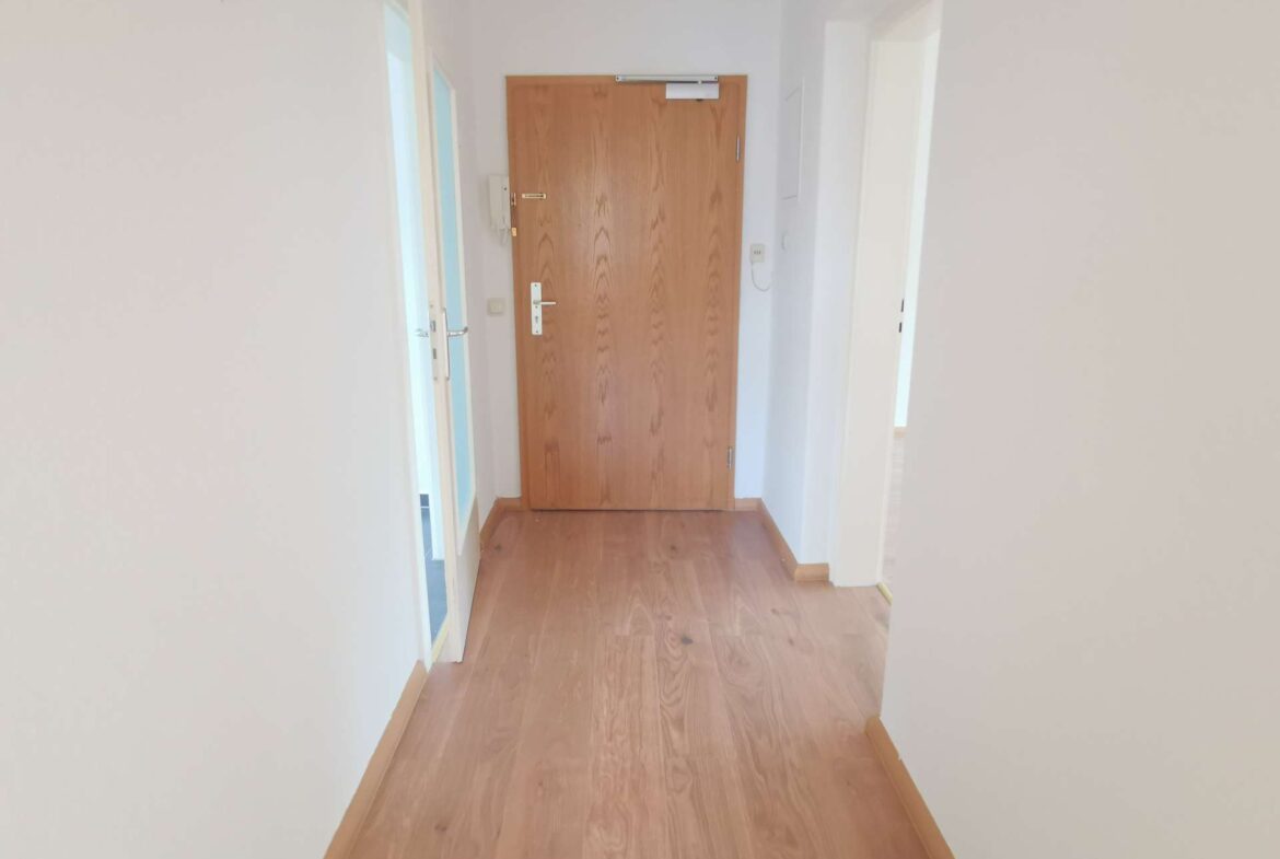 Narrow hallway with light walls, wooden floor, and a closed wooden door at the end.