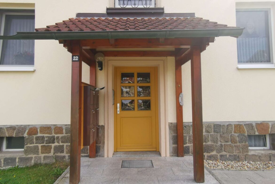 Yellow front door under a wooden porch with a tiled roof, beige walls, and stone foundation.