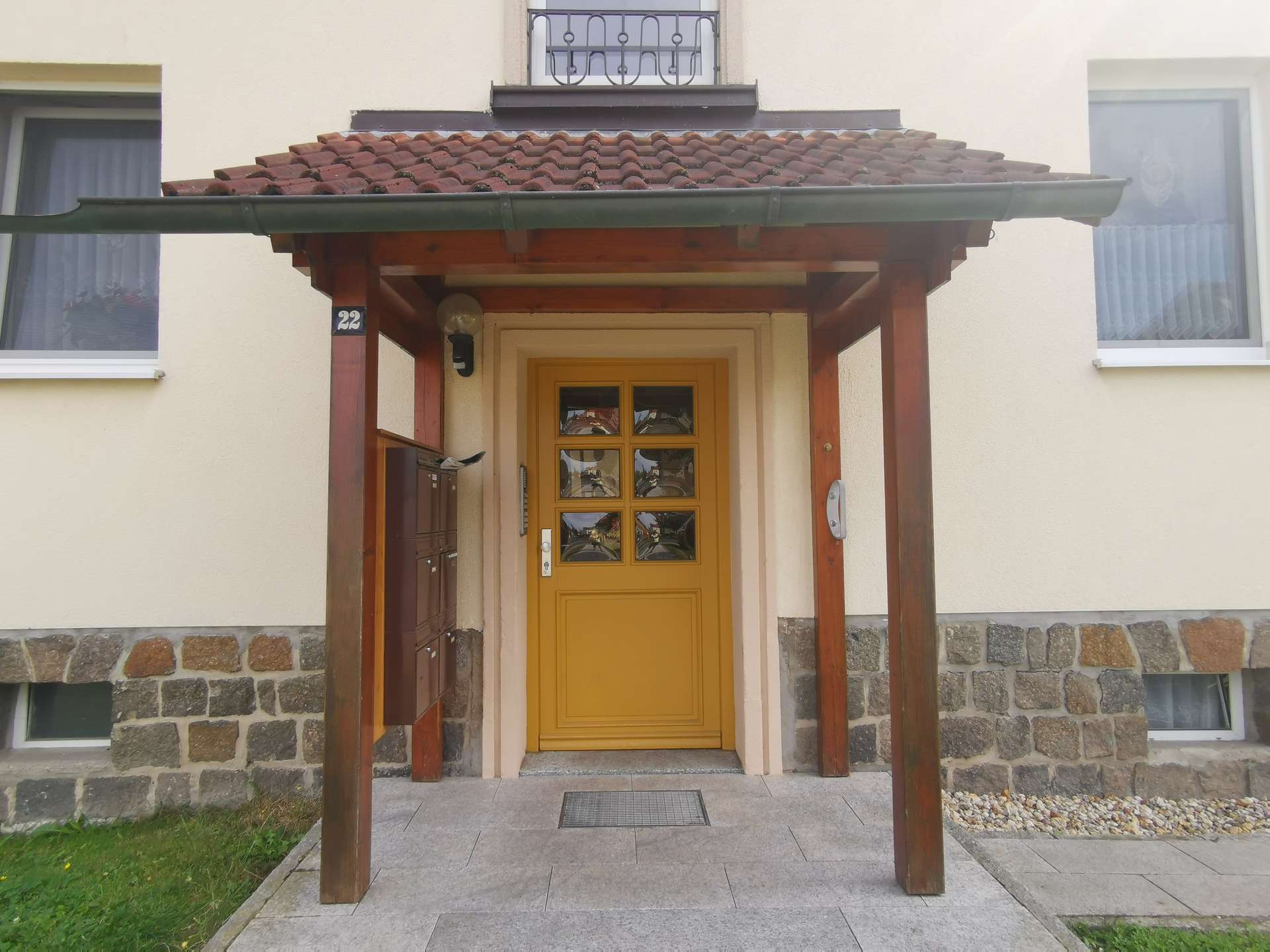 Yellow front door under a wooden porch with a tiled roof, beige walls, and stone foundation.