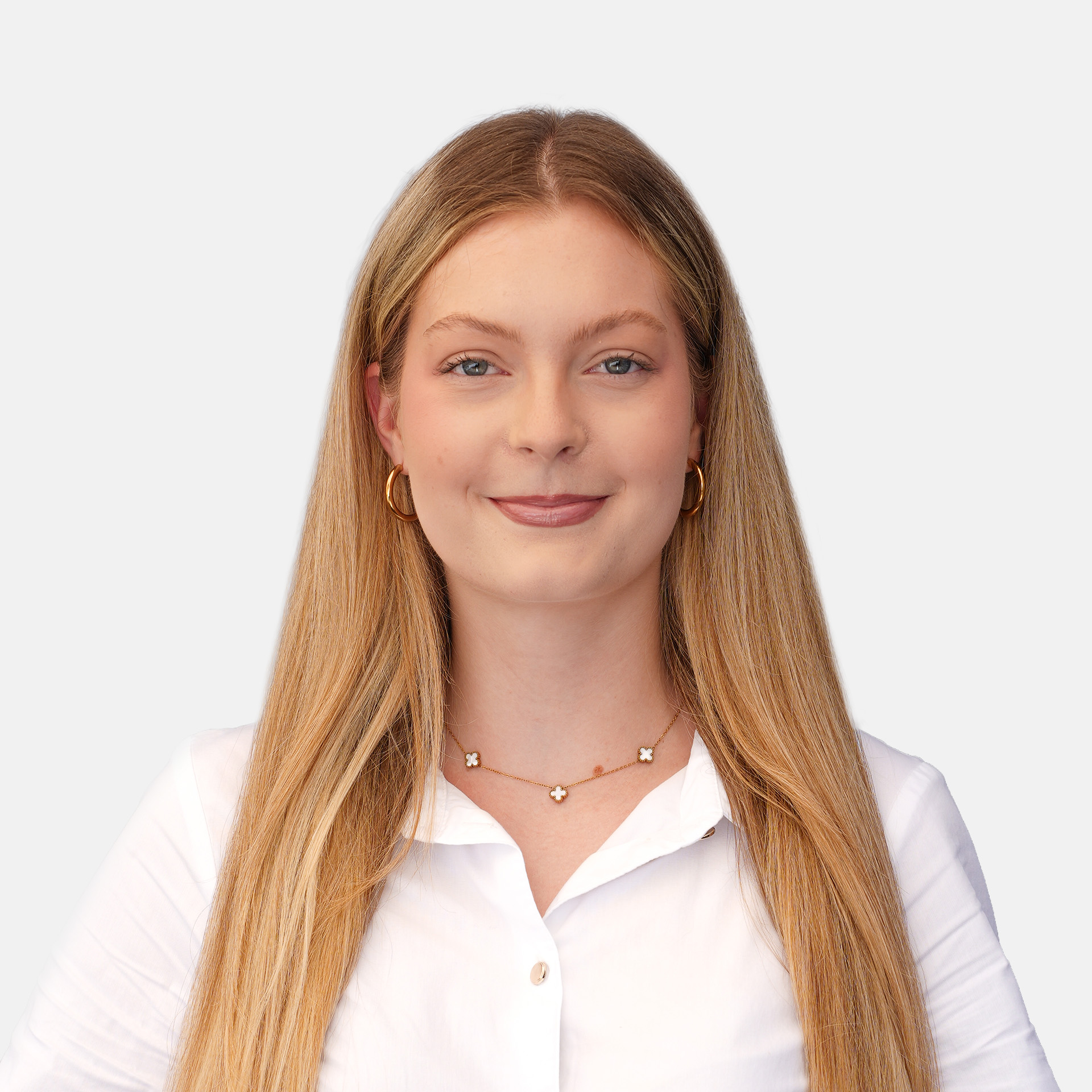 Close-up portrait of a smiling woman with long blond hair, wearing a white blouse and gold jewelry against a light gray background.