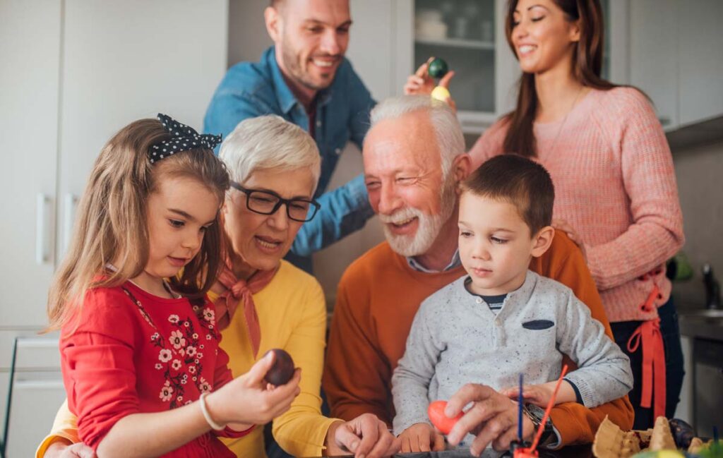 A multigenerational family in a kitchen dyeing Easter eggs together, smiling and focused on the activity.