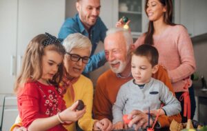 A multigenerational family in a kitchen dyeing Easter eggs together, smiling and focused on the activity.
